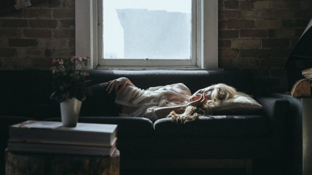 woman lying on sofa near closed window during daytime